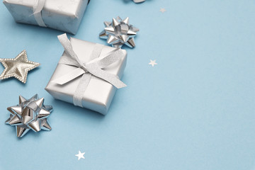 Gifts or present boxes in silver with silver bows and tree ball ornaments and little silver stars, table tob view. Composition for Christmas. Blue pastel background.