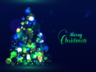 Green calligraphy text Merry Christmas and creative Xmas tree made by bokeh effect on blue background can be used as greeting card design.
