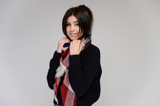 Close-up portrait of a young pretty girl student with long black hair with a scarf and in a sweater, on a white background. Standing right in front of the camera in different poses with emotions.
