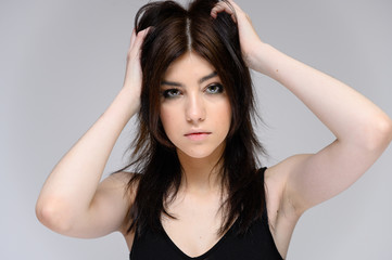 Fototapeta premium Close-up portrait of a young pretty girl with long black hair, clean skin on a gray background. The concept of cosmetics for the face, great makeup, fashionable hairstyle.