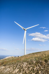 View of a wind turbine on top of mountains, blue sky as background