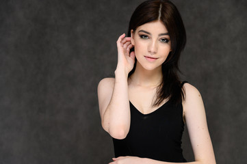 Close-up portrait of a young pretty girl student with long black hair, on a gray background. He stands right in front of the camera, showing his hands in different poses with different emotions.