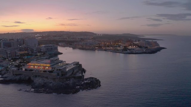 High Aerial shot orbiting around the coast of St Julians Malta. Baech at the sunset