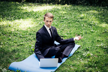 Man in a suit with tie. Business man relaxing in a park in the lotus position, he can't relax in...