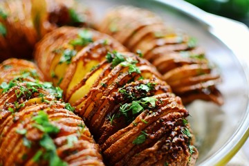 Appetizing potato accordion baked in the oven. Potato on a wooden background.  Hasselback potatoes.  Vegan food, vegetables with parsley and garlic