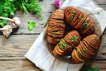 Obraz na płótnie Canvas Appetizing potato accordion baked in the oven. Potato on a wooden background. Hasselback potatoes. Vegan food, vegetables with parsley and garlic