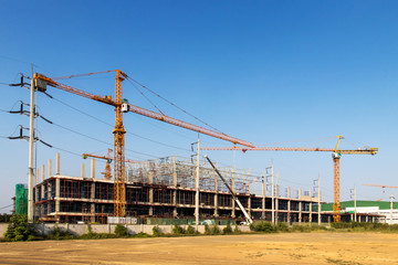 A construction site including several cranes working on a building, Boom crane on the construction of a high-rise and scaffolding in the building,with blue sky background