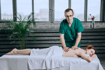 Massage therapist doing massotherapy of a young woman. Beautiful relaxed face of a young woman with brown hair and closed eyes.