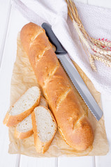 Freshly baked homemade french baguette with a brown crust on paper on a white wooden background.