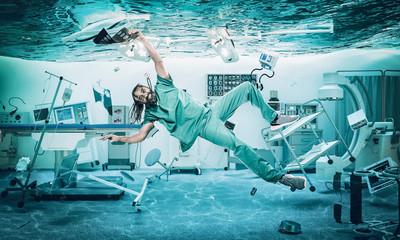Smiling doctor floats under water in a flooded operating room.