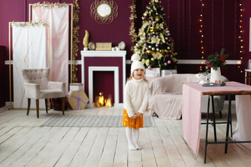 Cozy little sister children in white warm sweaters and knitted hats in the Christmas interior, con