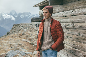 Handsome male model wearing warm sweater and winter coat over mountains with snow