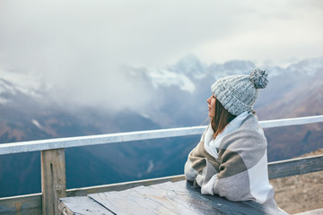 Teenage girl wrapped in plaid blanket sitting by table on mountain top