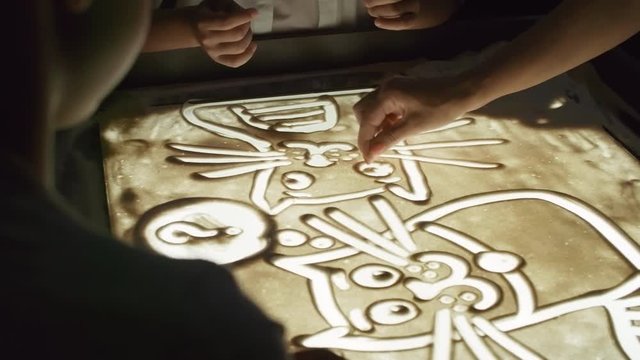 Tilt up shot of unrecognizable art teacher helping children making sand animation on light table