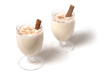 Eggnog Christmas cocktail in a transparent wine glass, decorated with cinnamon stick, sprinkled with grated nutmeg. Isolated on white background. Copy space.