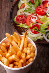 French fries chips crispy potatoes in white bowl and vegetable salad on wooden background.