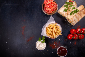 Fast food. Red bowl of french fries chips potato and sauces, doners on black background. top view, copy space