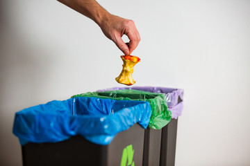 Hand putting apple stub in recycling bio bin. Person in a house kitchen separating waste. Black...