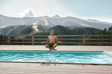 Young guy spending vacation in swimming pool with mountain landscape