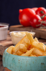 Blue bowl of french fries chips potato and sauces on black background. fast food. tomatoes on background