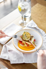 Roasted Halibut with vegetables, paprika pepper and pumpkin cream. Lunch in a restaurant, a woman eats delicious and healthy food. Dish decorated with a slice of lemon. Restaurant menu