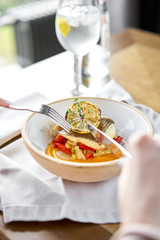 Roasted Halibut with vegetables, paprika pepper and pumpkin cream. Lunch in a restaurant, a woman eats delicious and healthy food. Dish decorated with a slice of lemon. Restaurant menu