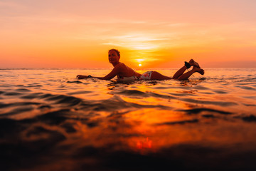 Attractive surfer woman on a surfboard in ocean. Surfgirl at sunset