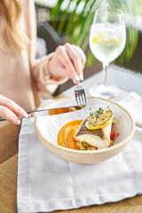 Roasted Halibut with vegetables, paprika pepper and pumpkin cream. Lunch in a restaurant, a woman eats delicious and healthy food. Dish decorated with a slice of lemon. Restaurant menu