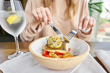Roasted Halibut with vegetables, paprika pepper and pumpkin cream. Lunch in a restaurant, a woman eats delicious and healthy food. Dish decorated with a slice of lemon. Restaurant menu