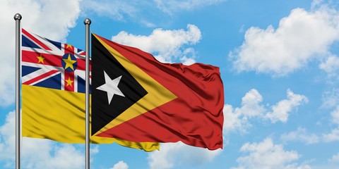 Niue and East Timor flag waving in the wind against white cloudy blue sky together. Diplomacy concept, international relations.