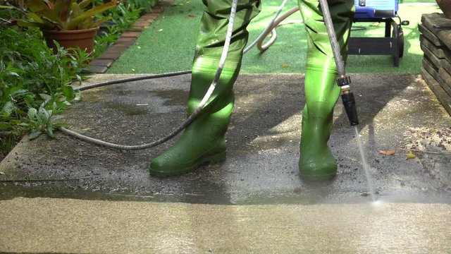 High pressure cleaning ,lower body with waterproof boots. Worker cleaning dirty floor in backyard with high pressure washer splashing the dirt ,4K timelapse .  Professional cleaning services.