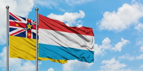 Niue and Luxembourg flag waving in the wind against white cloudy blue sky together. Diplomacy concept, international relations.