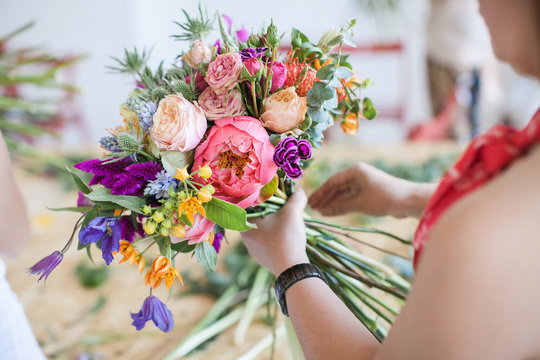 Woman holding a bouquet of roses, peonies, hyacinth, thorn and other flowers. Education. Florist communication with customer in the workshop in the studio with flowers.