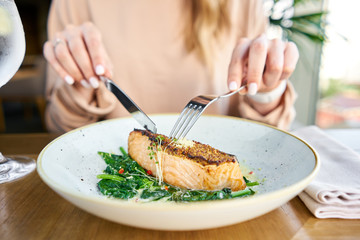 Salmon steak fillet with grainy mustard and spinach. Lunch in a restaurant, a woman eats delicious...