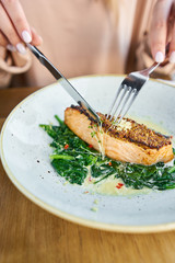 Salmon steak fillet with grainy mustard and spinach. Lunch in a restaurant, a woman eats delicious and healthy food. Restaurant menu, a series of photos of different dishes