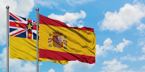 Niue and Spain flag waving in the wind against white cloudy blue sky together. Diplomacy concept, international relations.