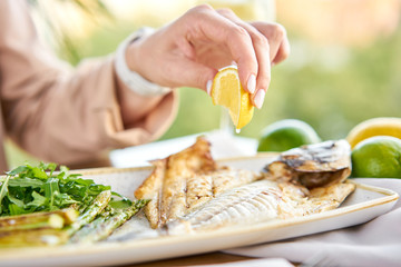 Lunch in a restaurant, a woman eats roasted dorado fish with grilled asparagus. Dish decorated with a slice of lemon. Restaurant menu