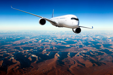 White passenger plane in flight. The plane flies against a background of mountain landscape....