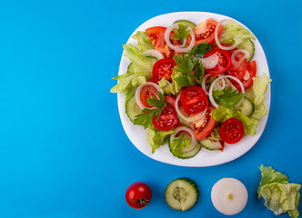 Vegetable salad of white onion, cucumber, tomatoes, lettuce, parsley on blue background. Low carb dietary food. Top view. Copy space