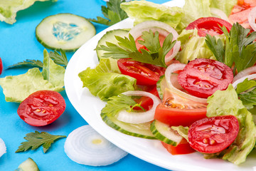 Vegetable salad of white onion, cucumber, tomatoes, lettuce, parsley on blue background. Low carb dietary food. Top view.