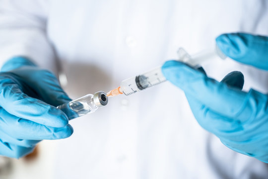 Nurse or doctor hand in blue glove holding flu, measles vaccine vial and syringe wiht needle for baby vaccination, medicine and drug concept