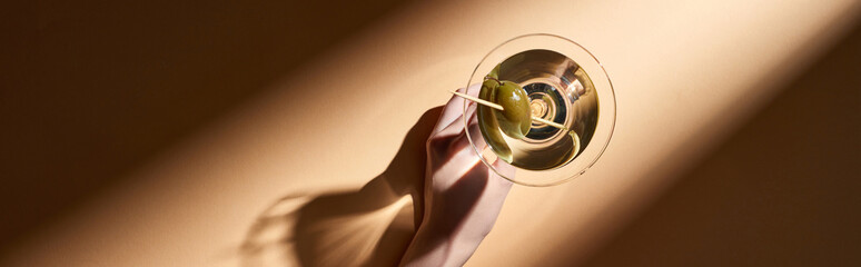 Cropped view of woman holding in hand glass of martini on beige background, panoramic shot