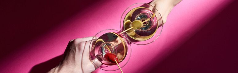 Cropped view of man and woman holding martini cocktails on pink background, panoramic shot