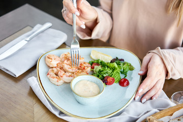 Grilled Argentine shrimp with mango-jalapeno sauce. Lunch in a restaurant, a woman eats delicious and healthy food. Delicious fresh seafood prawns with fresh vegetables and lime. Cream sauce