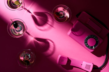 Top view of martini cocktails and retro telephone on pink background