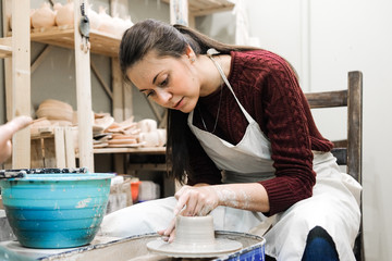 Sculptor woman makes a cup on a potters wheel.