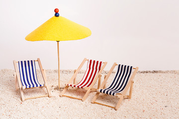 Toy chaise longue and sun umbrella on sandy beach on sunny day at the white background. Relaxation concept.
