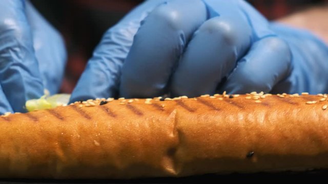Extra close-up of a cook's hands preparing a hot dog, he puts a leaf of salad inside a bun