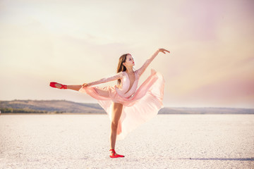 girl ballerina dancer in a pink dress on a snow-white salty dried lake. Fantastic landscape and a girl in red punata and a pink dress.