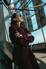 elegant young woman posing in trendy burgundy suit and sunglasses on urban roof